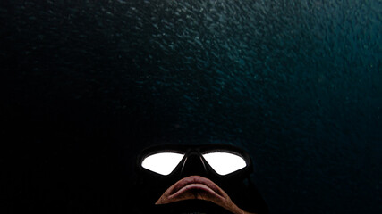 Close up on a free diver ascending to the surface. Massive school of fish in the background.