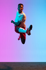 Obraz premium One African man, professional soccer football player training isolated on gradient blue pink background in neon light. Front view