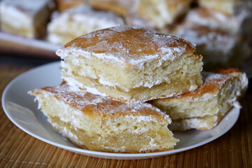 Lemon pie with powdered sugar in white plate on a table. Pieces of homemade sweet cake on a kitchen