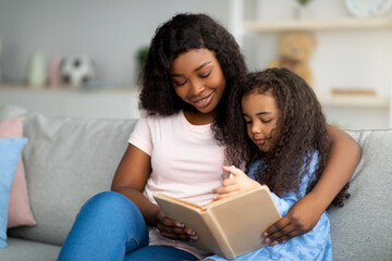 Family stay home hobbies. Millennial black mother and her cute daughter reading book together at home