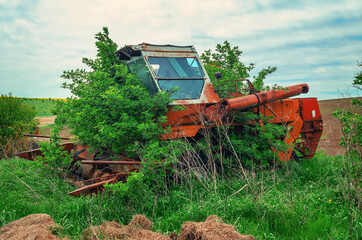 Old abandoned rusty combine overgrown with bushes on the field
