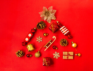 Flat composition with a Christmas tree made of different festive items, snowflakes, gifts, sweets, Christmas tree decorations on a red background. Copy space.