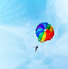 Two men are sailing on a colorful and bright parachute against the blue sky. Copy space.