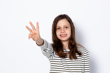 A funny dark-haired girl shows three fingers on her hand. Digit 3. Portrait on a light background. Place for your text.