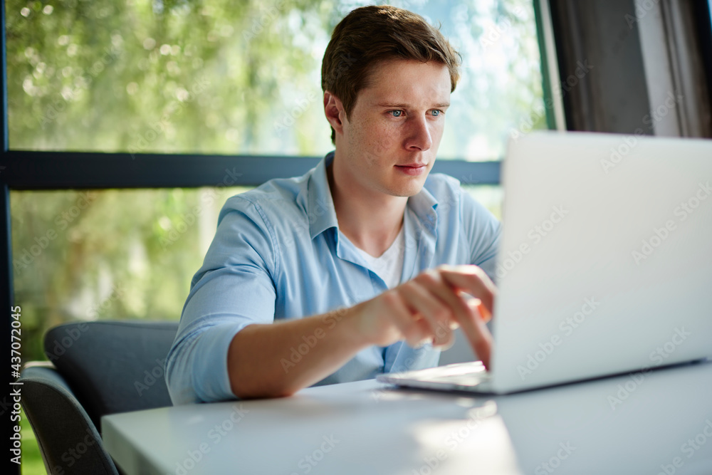 Poster young hipster guy searching web or text content in social media using laptop computer indoors, skill