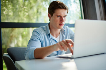 Young hipster guy searching web or text content in social media using laptop computer indoors, skilled male IT professional checking update settings on netbook while doing online distance job