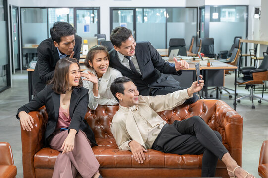 Cheerful asian colleagues greeting with selfie by smartphone on leather sofa in coworking space - Powered by Adobe
