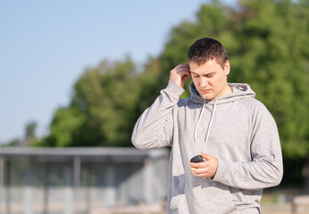 Young man puts on wireless headphones outdoors. Active lifestyle concept.