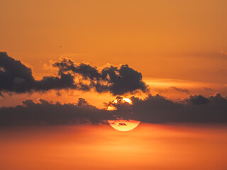 Sun behind small clouds in orange sky near sunse