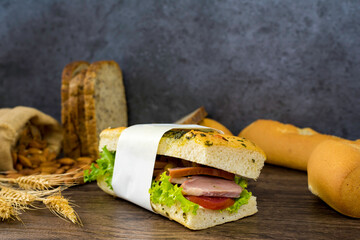 Sandwich sandwich with ham Fresh green lettuce Red tomatoes Have French bread Almonds in sacks and wheat grass put together on wooden boards.