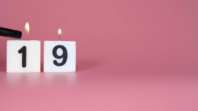 A square candle saying the number 19 being lit and blown out on a pink background celebrating a birthday or anniversary