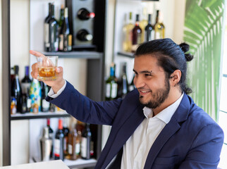 latin man in suit raising a glass of whiskey in toast