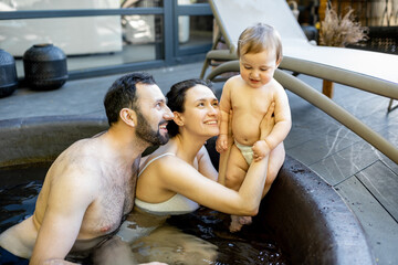 Young family relaxing with a little baby boy at spa, sitting in the hot vat outdoors. Family on vacation with a child