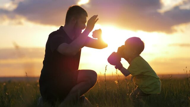 Family Training. Silhouette father and little son teaches boxing during in summer warm sunset time. Young dad trains his little son, teaches him to box. Concept childhood sports motivation.