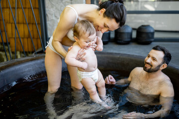 Young family relaxing with a little baby boy at spa, sitting in the hot vat outdoors. Family on...