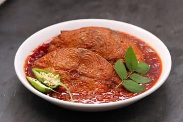 Seer Fish curry, traditional Indian fish curry ,kerala special ,arranged in a white bowl garnished with curry leaves and fresh  chilli on a grey textured background,isolated.