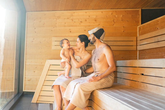 Young family resting with a little baby boy in sauna. Family vacation with one year child in spa