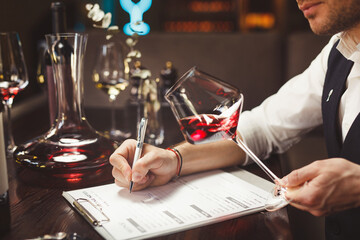 Expert writes holding glass of expensive red wine at table