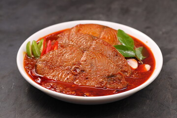 Seer Fish curry, traditional Indian fish curry ,kerala special ,arranged in a white bowl garnished with curry leaves and fresh  chilli on a grey textured background,isolated.