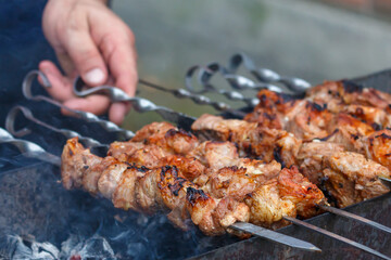 Cooking meat on coals outside. Male hand holding shish kebab close-up, selective focus.