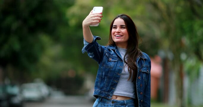 Young woman holding smartphone taking selfie outdoors