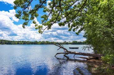 A landscape crop of a Wisconsin Lake (Lower Genesee Lake in Waukesha County).  A swimming raft floats on the calm waters while cumuls clouds are reflected. - obrazy, fototapety, plakaty