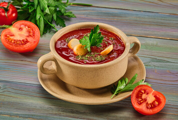 Tomato soup puree with croutons, spices and herbs in a brown tureen. Fresh tomatoes, a bunch of parsley on a wooden table. Background image, copy space