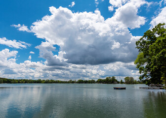 A landscape crop of a Wisconsin Lake (Lower Genesee Lake in Waukesha County).  A swimming raft floats on the calm waters while cumuls clouds are reflected.