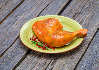 Fried chicken leg with a golden crust on a light green plate with pink pepper and rosemary on a wooden table. Background image, copy space