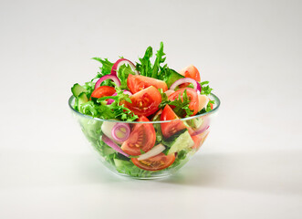 Healthy food. Vegetable salad in a transparent bowl. Salad of red tomatoes, cucumbers, red onions, green lettuce leaves, garlic with olive oil on a white background. Background image, copy space