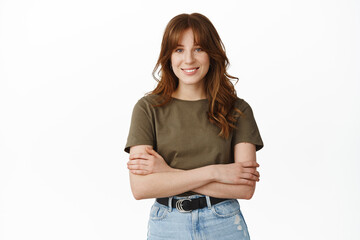 Portrait of confident girl with crossed arms, look determined and ready, smiling with white teeth, standing in t-shirt and jeans against white background