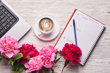 Flat lay women's office desk. Female workspace with laptop, pink peonies bouquet and coffee on white background. Top view feminine background.