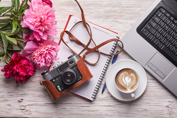 Flat lay women's office desk. Female workspace with laptop, pink peonies bouquet, camera and coffee on white background. Top view feminine background.