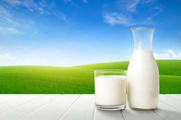 Glass and bottle of fresh milk on white wooden table with green meadow background.