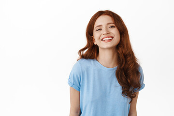 Beautiful redhead woman smiling with white perfect teeth, showing happy face emotion, standing in casual blue t-shirt against white background
