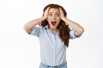 Surprised ginger girl gasp, look in awe and amazement, holding hands on head, checking out something awesome, being impressed by big news, standing against white background