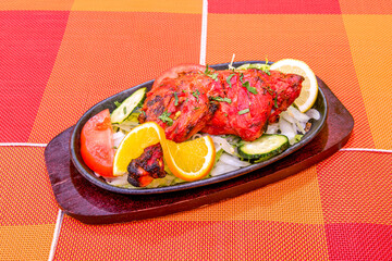 Grilled chicken thigh in Hindu tandoori style with bright red color and charred grill marks on hot plate - obrazy, fototapety, plakaty
