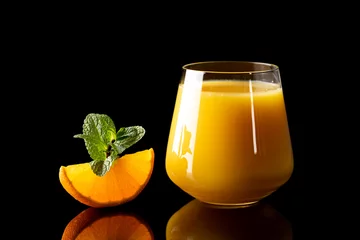 Fotobehang fresh orange juice into glass goblet on black background © Alexander Gogolin