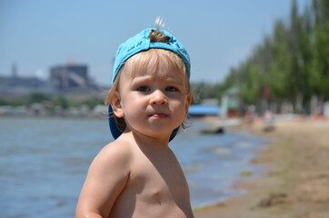 Little blond toddler boy on the beach play with sand and toys near the sea. Copy space. Summertime. Close up. Sea view. Sunshine. 