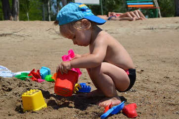 Little blond toddler boy on the beach play with sand and toys near the sea. Copy space. Summertime. Close up. Sea view. Sunshine. 