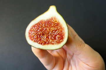 half of juicy red figs inside in the right hand of a woman on a black background top view. fruit...