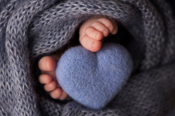 Two cute tiny baby feet wrapped in a blue-green aqua knitted blanket. And a knitted heart made of woolen threads.