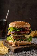 fast food. a large juicy burger with beef patty, iceberg lettuce, tomatoes, pickles, onions and sauce and bacon slices. Low key, dark mood