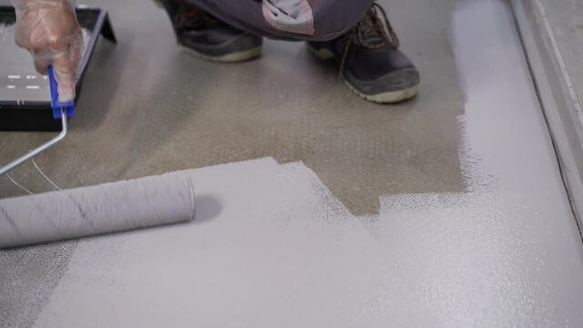 The process of applying a white polymer coating to the floor. Rolling Epoxy Paint on Concrete Floor. Closeup applying primer on the floor.