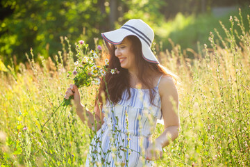 Young woman picking flowers in the meadow in summer evening