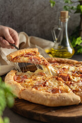 selective focus. hot pizza with cheese and pepperoni. the girl pulls a slice of pizza with melted cheese stretching. vertical position, dark mood