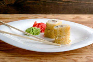 baked sushi stacked on top of each other in two piles with eel wasabi ginger and chopsticks on a white plate