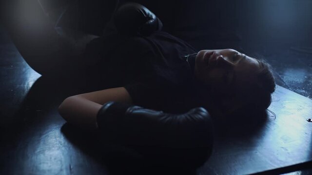 A Woman Wearing Boxing Gloves Lies Exhausted On The Floor After A Workout