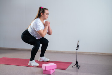 A chubby young woman is watching an online fitness lesson on a mobile phone. Distance sports...