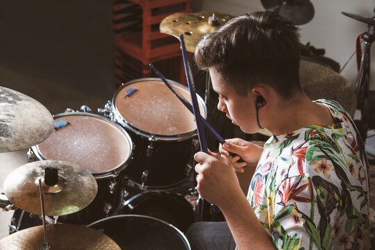 teenager boy drummer playing on rehearsal in a studio. rock musician male teen performing a song. rear view